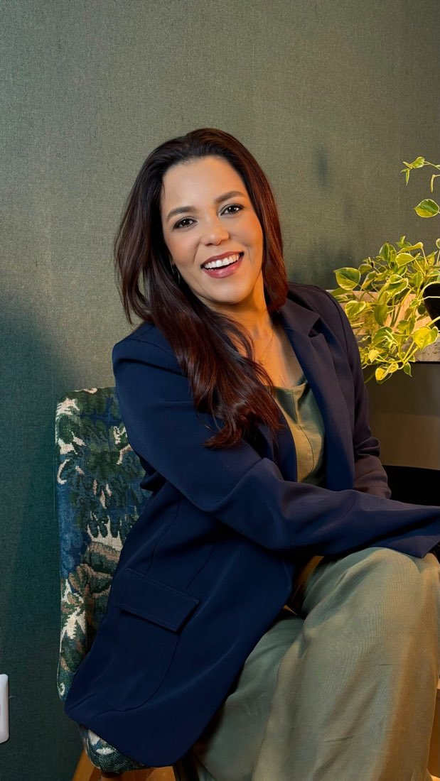 Designer de blazer azul sentada numa poltrona estampada, vídeo sobre reforma da Ana Paula Lima Interiores